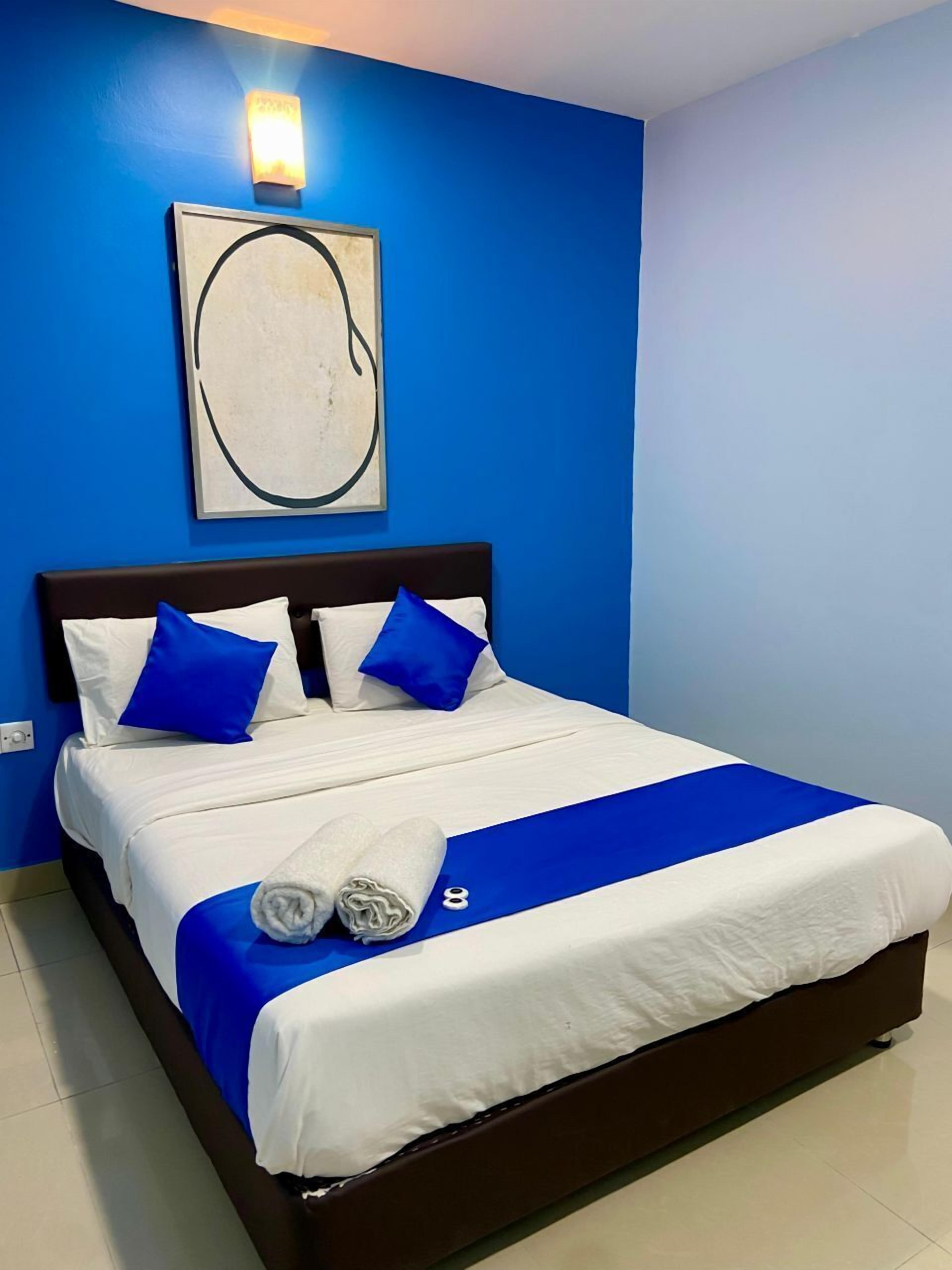 Una cama bien tendida con ropa de cama azul y blanca, una almohada decorativa azul y una toalla al lado.