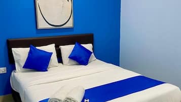 Una cama bien tendida con ropa de cama azul y blanca, una almohada decorativa azul y una toalla al lado.