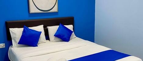 Una cama bien tendida con ropa de cama azul y blanca, una almohada decorativa azul y una toalla al lado.