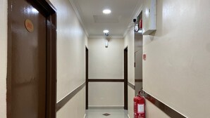 A hallway with a fire extinguisher mounted on the wall, a door with a sign, and a ceiling light. - Royals Star Hotel (Seremban)