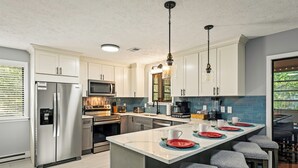 Cozinha moderna com eletrodomésticos de aço inoxidável, uma ilha central com banquetas e vista para o exterior.