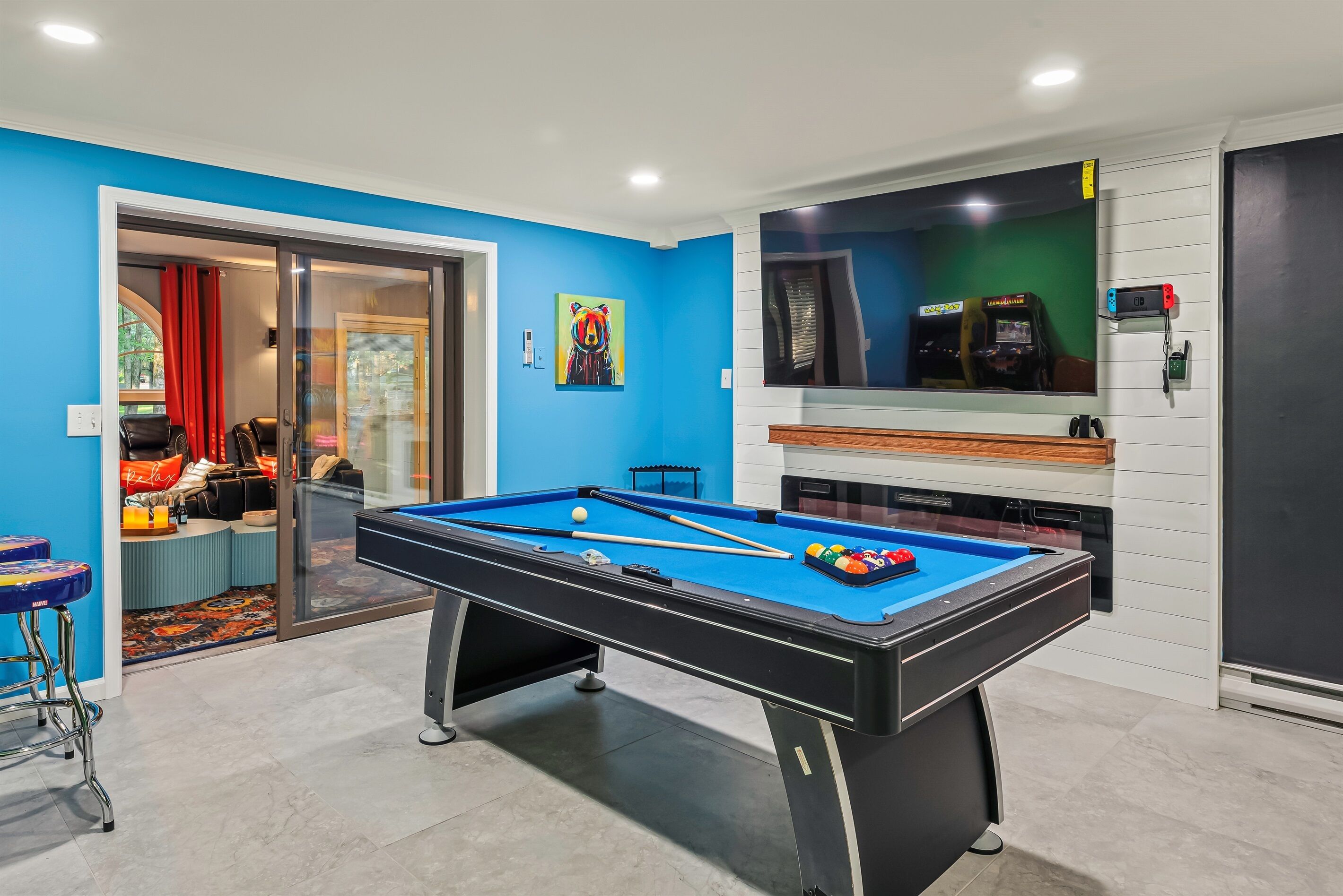 A pool table in a room with blue walls, a large mirror, and a gaming console.