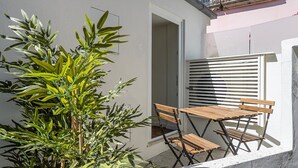 Un balcón con una mesa y sillas de madera, una planta en maceta y una ventana con persianas.