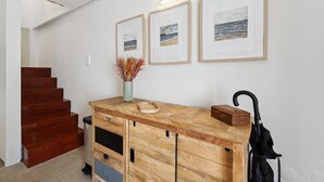Una consola de madera con un jarrón de flores secas, un paraguas negro y cuadros en una pared blanca.