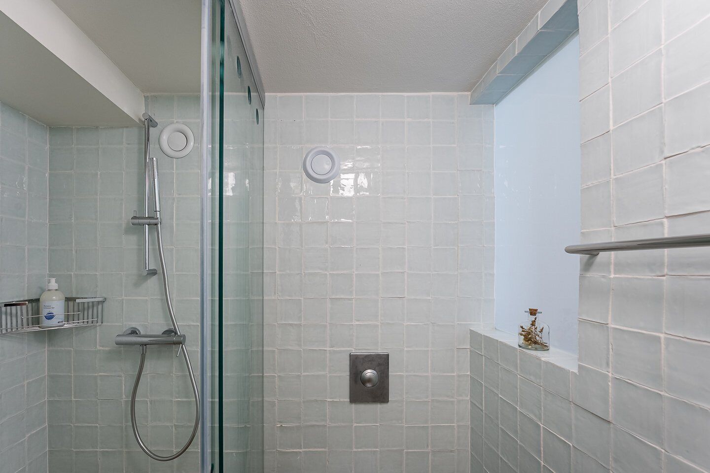 A modern bathroom with a glass shower enclosure, tiled walls, and a small shelf with toiletries.