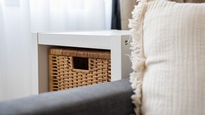 A white storage unit with a woven basket inside, placed on a grey sofa with a white throw blanket.