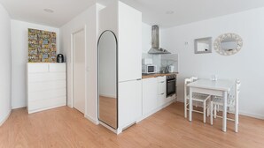 A compact kitchen with white cabinetry, a microwave, a kettle, and a stove. There's a dining table with chairs and a mirror on the wall.