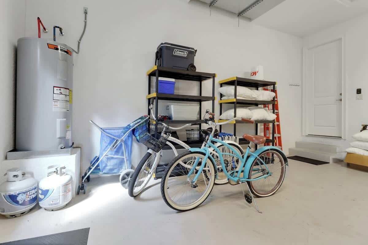 Een kamer met een boiler, gasflessen, een fiets, planken met tassen en een deur.