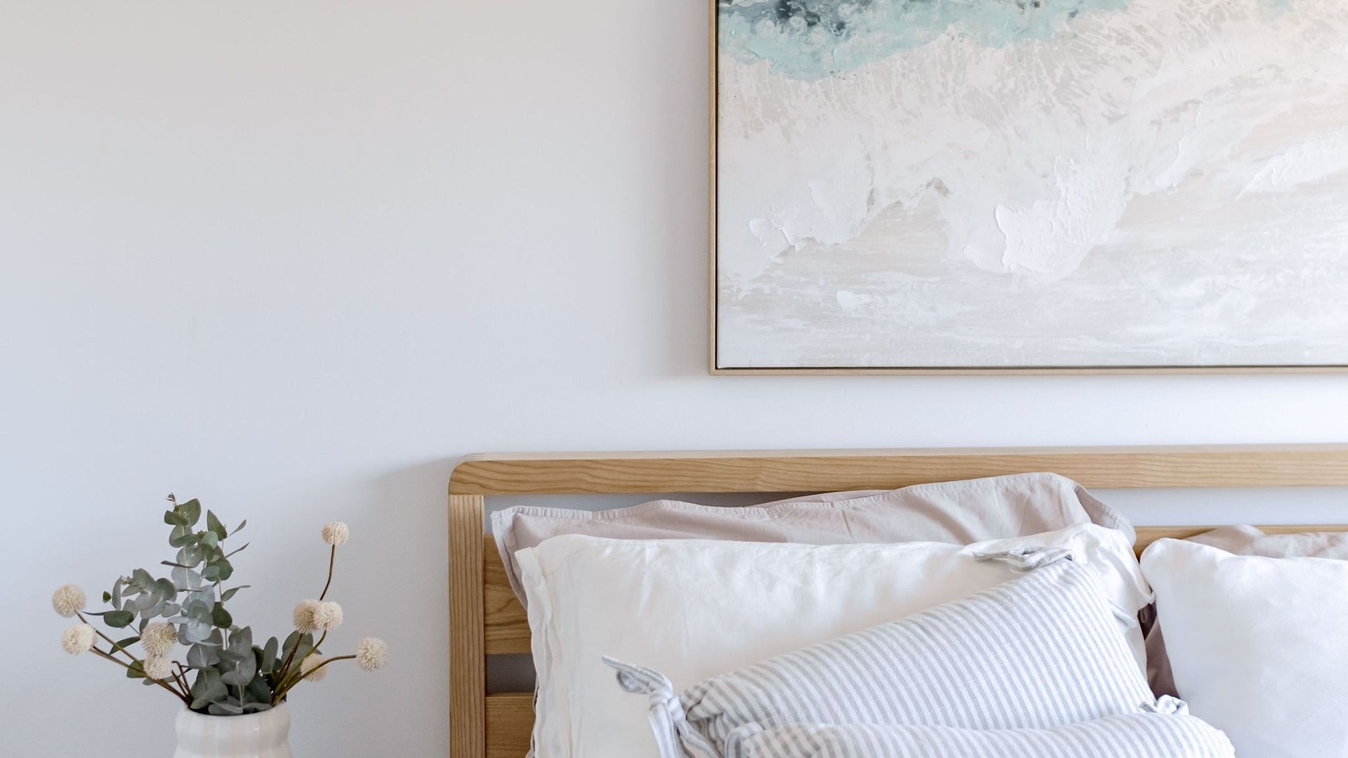 A bedroom with a wooden headboard, white bedding, and a framed abstract painting on the wall.