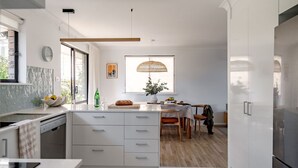 A modern kitchen with a central island, a dining area with a table and chairs, and a large window with a woven umbrella.