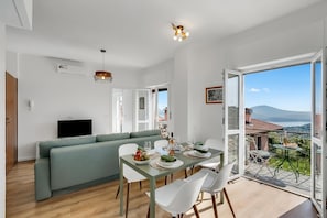 A modern living space with a dining area, a green sofa, and a balcony with a view.