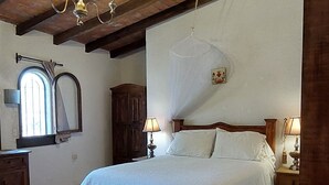 Une chambre avec un plafond en bois, un lit recouvert de draps blancs, une table de chevet en bois et une petite table.