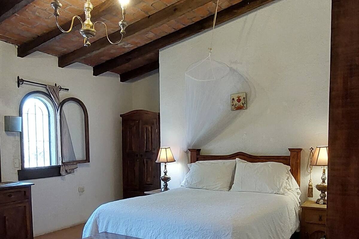 Ein Schlafzimmer mit Holzbalkendecke, einem Bett mit weißen Leinen, einem Nachttisch aus Holz und einem kleinen Tisch.