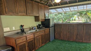 A kitchen with wooden cabinets, a stainless steel sink, and a refrigerator. - Charming Glamping Getaway (Pāhoa)