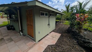A small, single-story building with a green exterior and a wooden door. It has a small porch area with a tiled floor and a few potted plants nearby. - Charming Glamping Getaway (Pāhoa)