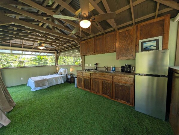 A compact kitchen with wooden cabinets, a refrigerator, and a bed with a table and chairs.