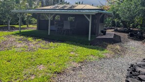 A small, single-story structure with a covered patio area, surrounded by a garden with various plants and trees. - Charming Glamping Getaway (Pāhoa)