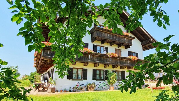 Un chalet traditionnel doté d’un balcon en bois, avec un vélo garé devant et une pelouse bien entretenue.