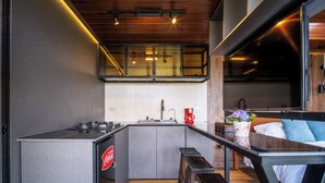 Een compacte keuken met een ingebouwde kookplaat, een koffieapparaat en een spoelbak. Er staan houten krukjes en een bank bij het aanrecht.