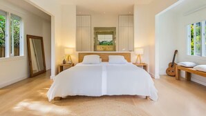 Ein geräumiges, helles Schlafzimmer mit einem Doppelbett, zwei Nachttischlampen, einem Deckenventilator und einem großen Spiegel über dem Bett.