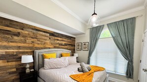 Ein Schlafzimmer mit Holzwandverkleidung, einem Bett mit Kissen, einem Nachttisch mit Lampe und einem Fenster mit Vorhängen.