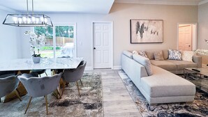 Ein modernes Wohnzimmer mit einer Couch, einem Esstisch mit Stühlen, einer Deckenleuchte und einem Bild an der Wand.