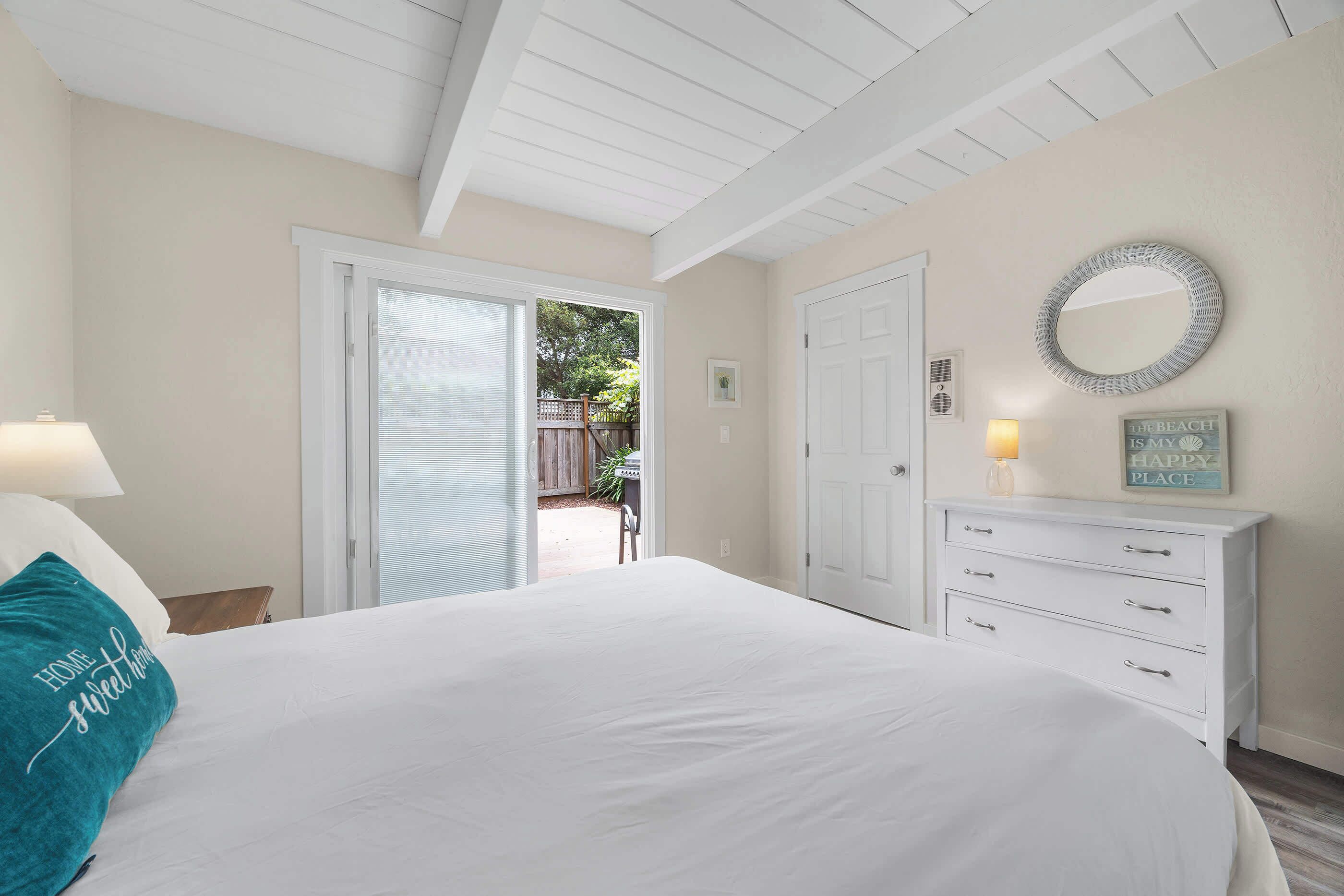 A bedroom with a bed, a dresser, a mirror, and a door leading to an outdoor area.