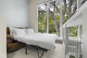 A bedroom with a bed, a brown chair, and a large window with a view of trees. - 3 Bedroom Home - Walking distance to beach! (Aptos)