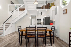 A dining area with a wooden table and chairs, a staircase, and a kitchen in the background. - 3 Bedroom Home - Walking distance to beach! (Aptos)