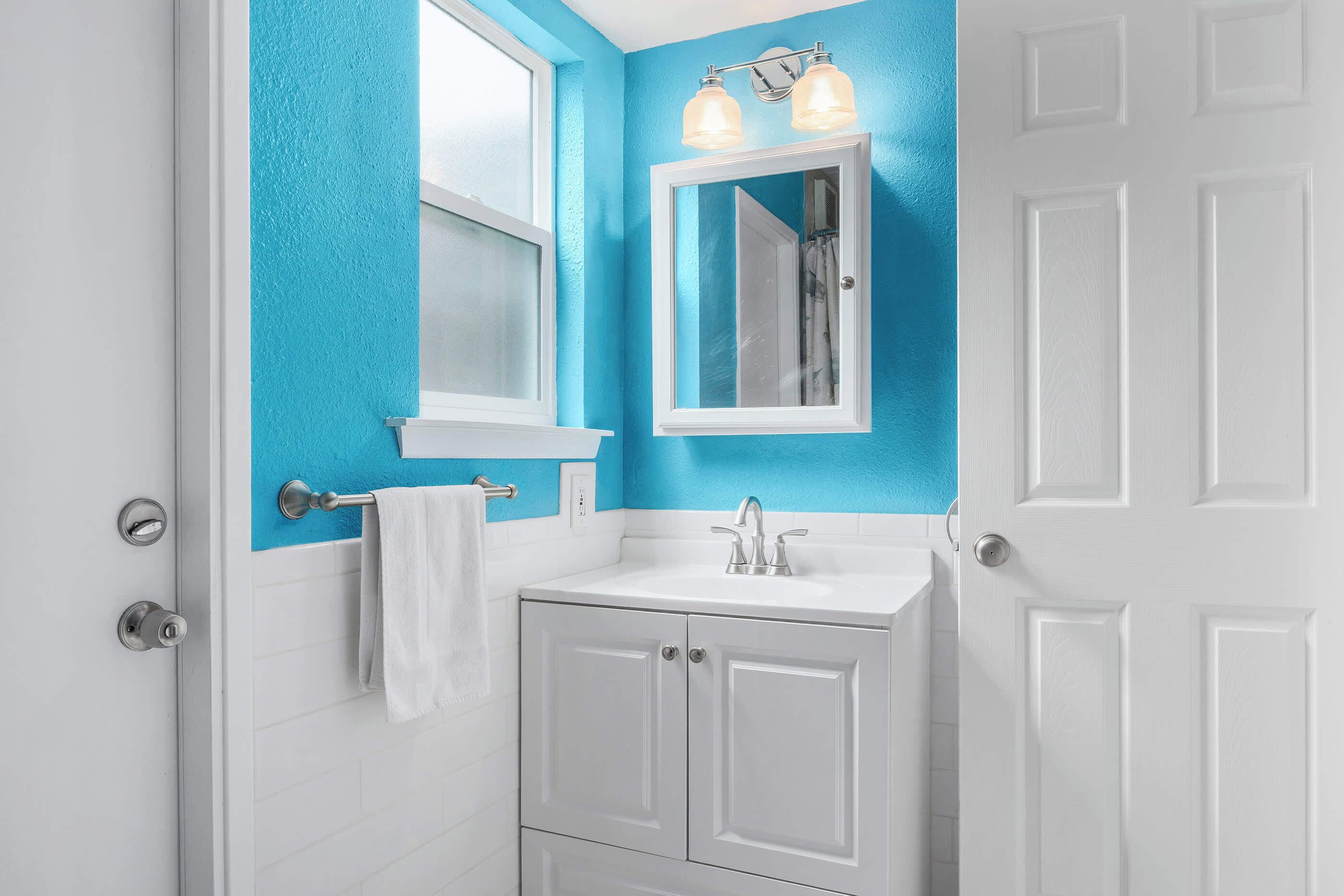 A bathroom with a white vanity, a blue accent wall, and a white door.