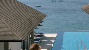 En kvinde ser ud over en pool med udsigt til havet og både.
