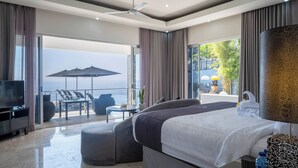 Et moderne hotelværelse med en stor seng, fjernsyn, en balkon med havudsigt og et spiseområde.