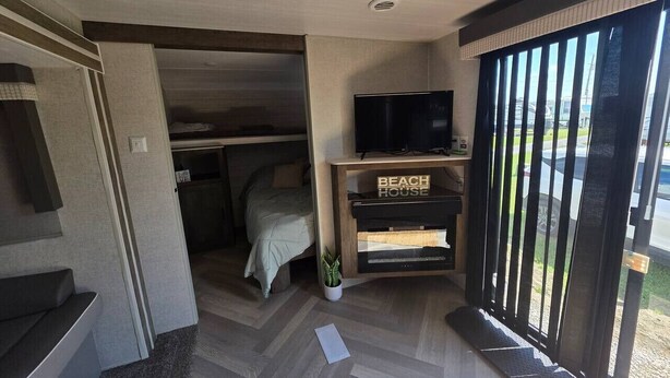 Ein kleines Zimmer mit einem Bett, einem Fernseher auf einem Holzbalken und einer Schiebetür zum Außenbereich.