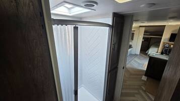Un pasillo estrecho que conduce a un dormitorio con un ventanal grande y una lámpara en el techo.