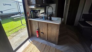 Eine kleine Küche mit Fensterblick, inklusive Spüle und Feuerlöscher.