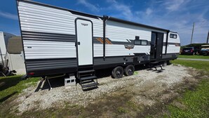 Ein weißer Wohnmobilwagen mit schwarzem Äußeren, einer Schiebetür und einer kleinen Stufe zum Eingang.