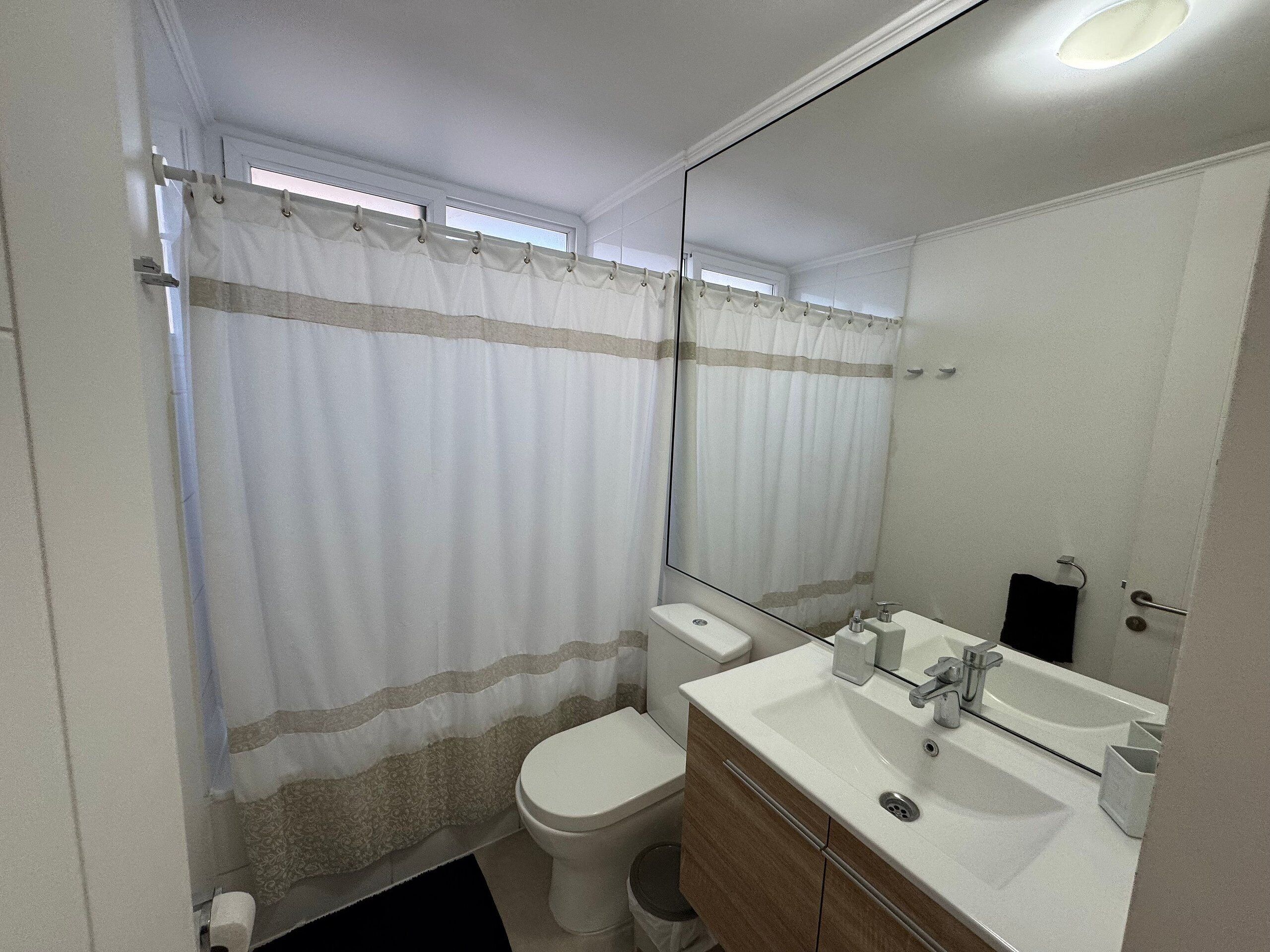 Een badkamer met toilet, wastafel, spiegel en douchegordijn.