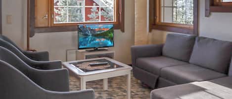 A living room with a sofa, two armchairs, a television on a stand, and a coffee table.