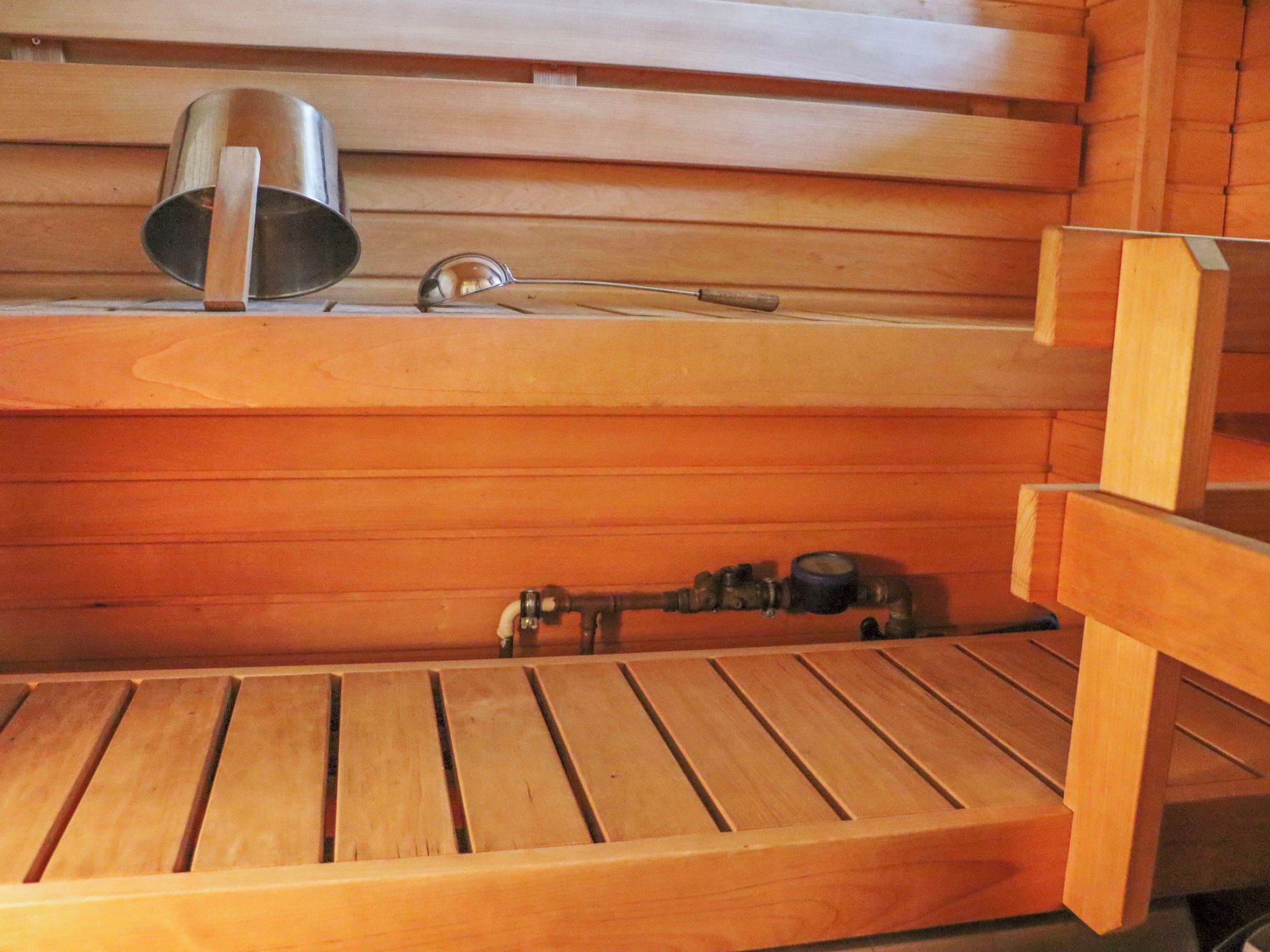 A wooden sauna with benches and a metal container on the upper shelf.