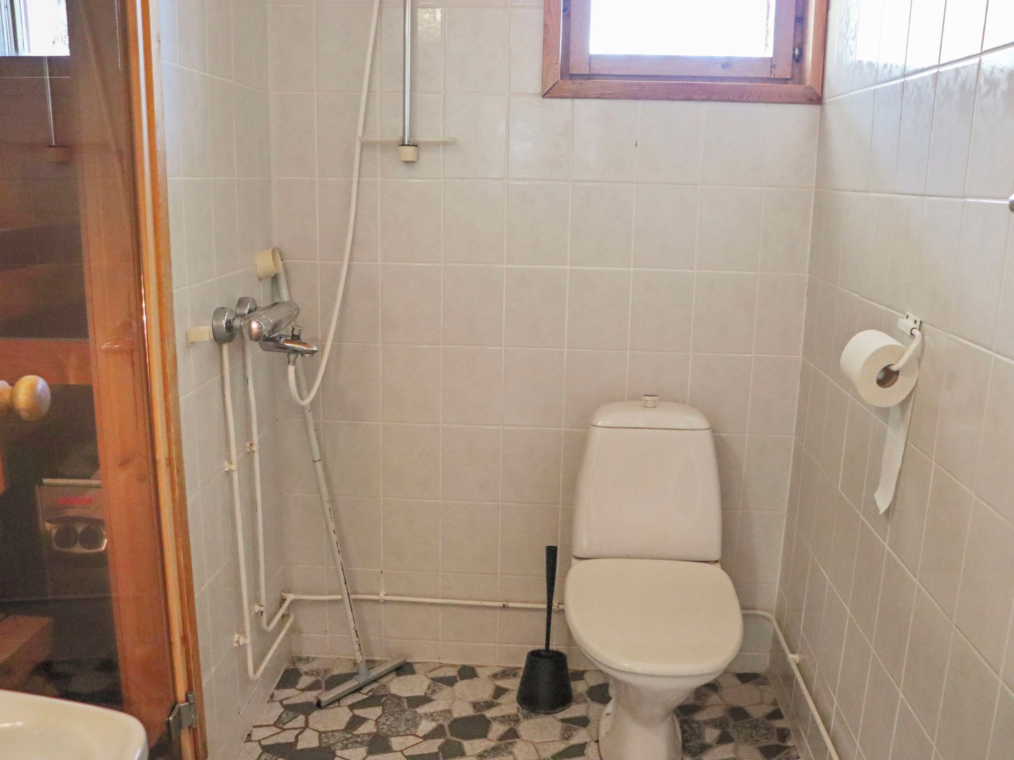 Un baño pequeño con inodoro, ducha y soporte para papel higiénico.