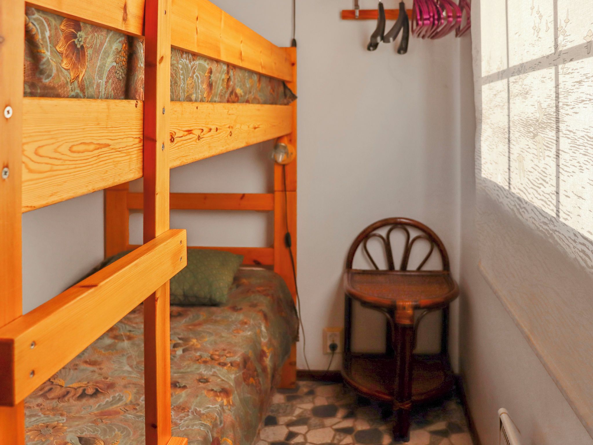 A bunk bed with a patterned mattress, a wooden chair, and a window with a view of the outside.