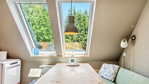 A room with a wooden table, a sofa, a hanging lamp, and a window with a view of trees.