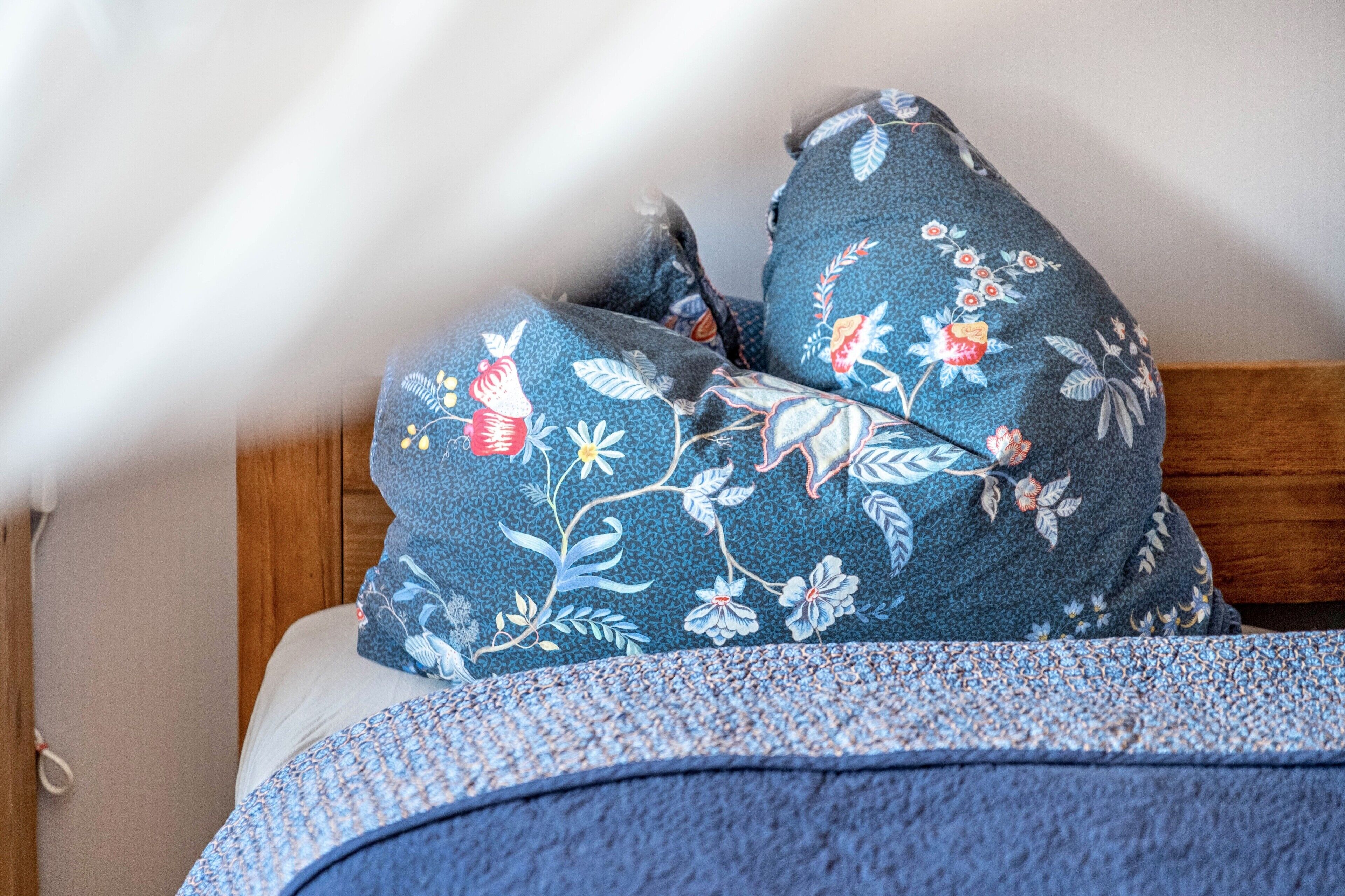 A bed with a floral-patterned pillow and a blue blanket.