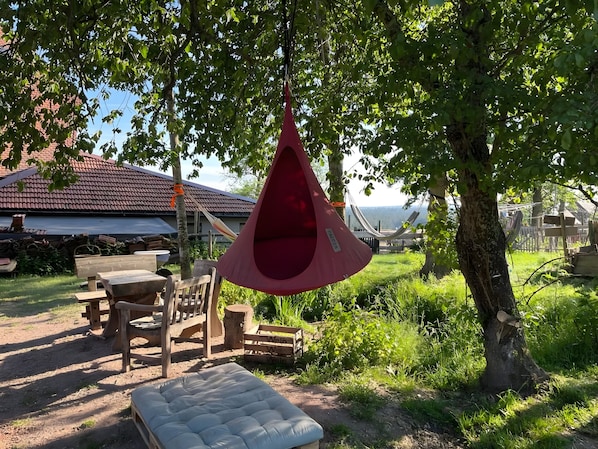 A hammock hanging from a tree, a wooden bench, and a mattress on the ground.