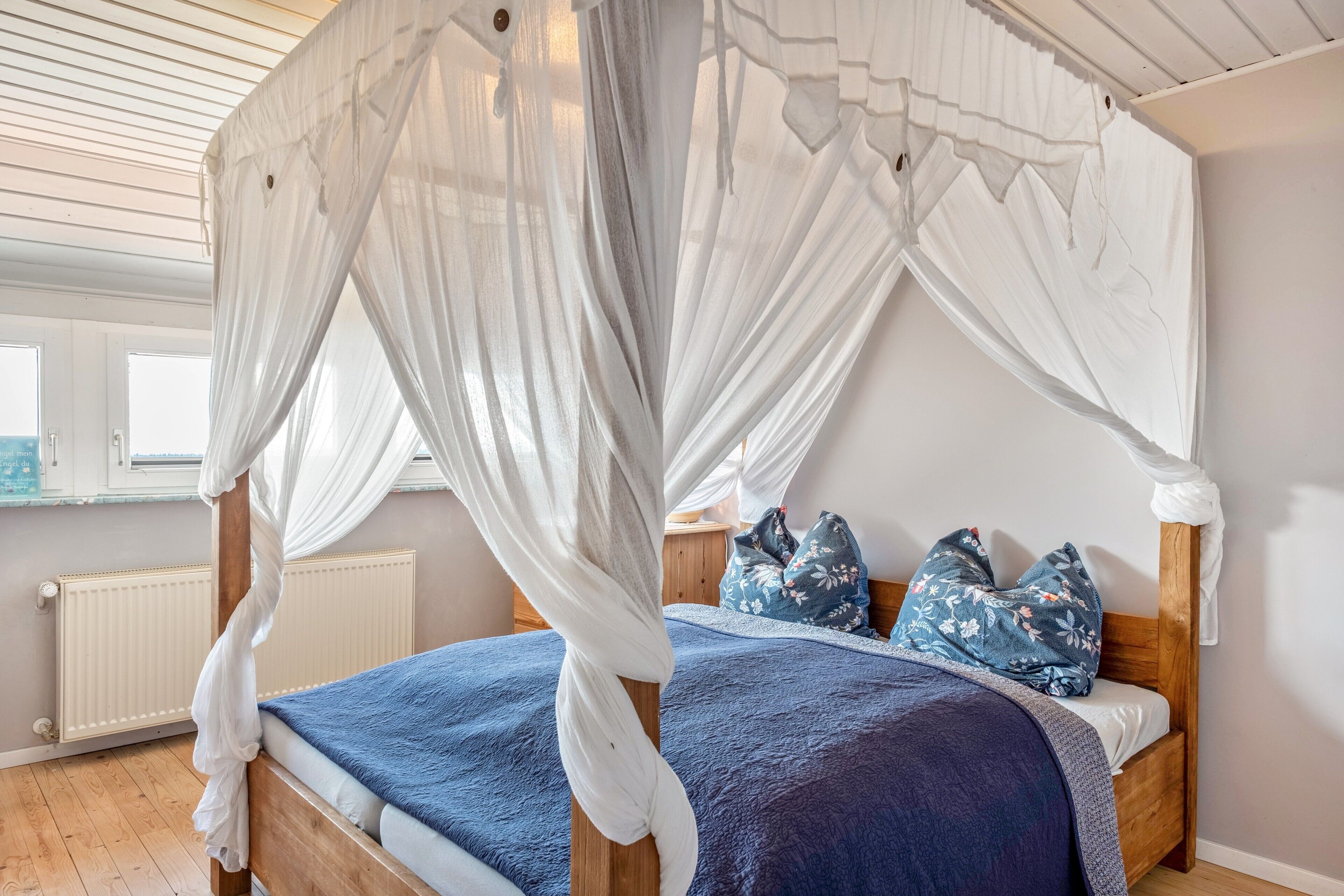 A bedroom with a four-poster bed, a wooden headboard, and a white canopy.