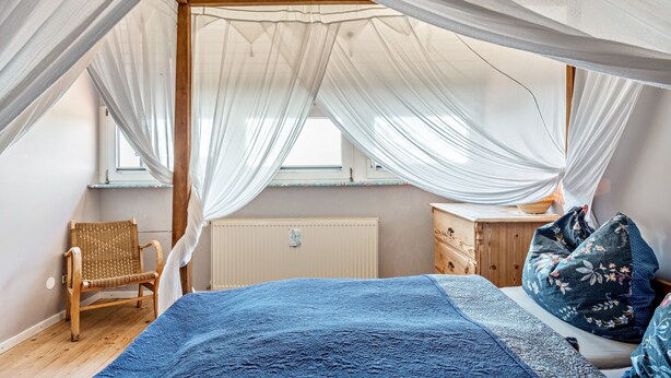 A bedroom with a canopy bed, a wooden chair, a dresser, and a window.