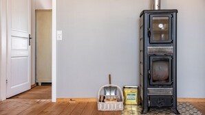 A room with a black wood-burning stove, a wicker basket, and a canister on the floor. - Apartment 'Rotkäppchen' with Shared Garden and Wi-Fi (Eisenbach (Hochschwarzwald))