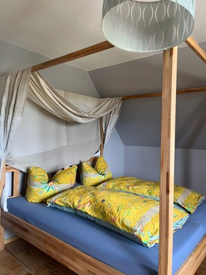 A wooden bed with a canopy, blue mattress, and yellow floral bedding. - Apartment 'Rotkäppchen' with Shared Garden and Wi-Fi (Eisenbach (Hochschwarzwald))
