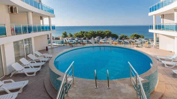 Un espace piscine offrant une vue dégagée sur la mer, agrémenté de chaises longues et d’une terrasse autour de la piscine.