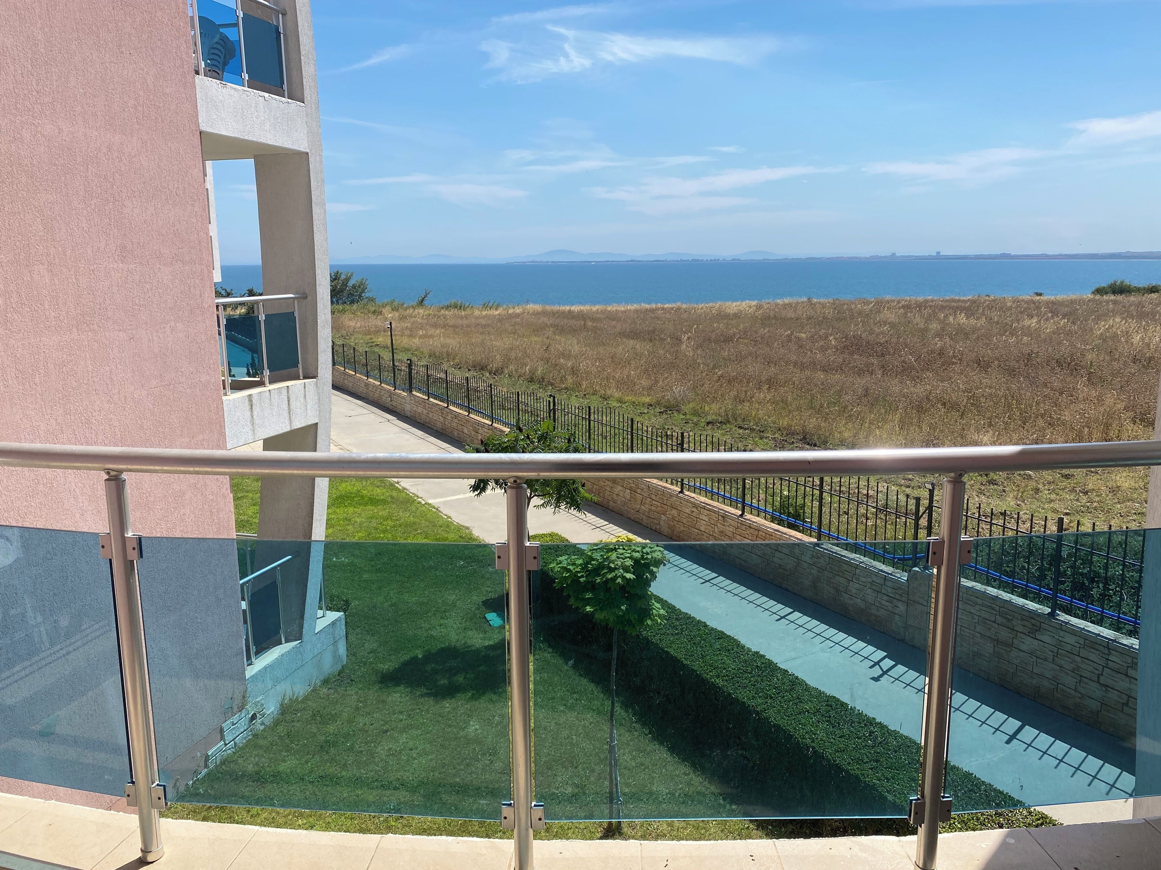 A balcony with a view of the sea and a grassy area.